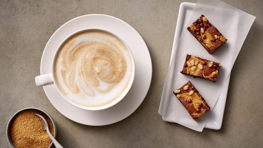 Tazza di cappuccino con dolcetti su un piatto e zucchero in una ciotola.